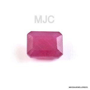 Könnte beinhalten: Ein facettierter, rechteckiger Rubin-Edelstein in tiefem Rosa. Der Edelstein ist vor einem weißen Hintergrund platziert. Der Text "MJC" befindet sich über dem Edelstein. Der Text "MAYZAHJEWELLERSCO." steht darunter.