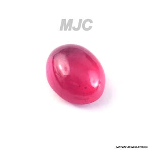 May include: A polished, oval-shaped, ruby-coloured gemstone. The gem has a smooth, glossy surface against a white background. The letters "MJC" are in the upper centre. The text "MAYZAHJEWELLERSCO." is in the lower right corner.
