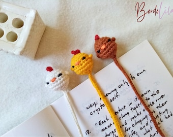 May include: Three handmade crochet animal bookmarks. One is white with a red accent, one is yellow with a red accent, and one is brown with an orange accent. The bookmarks are on a page with handwritten text. The brand name "Bordolila" is written in cursive.