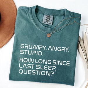 May include: A white ceramic mug with a black handle and the text "But First, Coffee" in a bold, black font. The mug is set against a neutral background, highlighting its simple design.