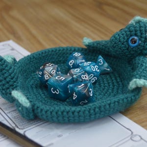 Pu&ograve; includere: Un vassoio da gioco per dadi a forma di drago in crochet color turchese con un corno bianco e un occhio nero. Il vassoio &egrave; pieno di dadi blu e bianchi con i numeri 3, 4, 5, 6, 8, 10, 20 e 30.