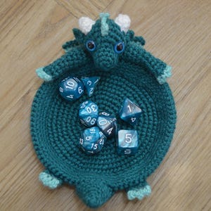 Pu&ograve; includere: Un vassoio da gioco per dadi a forma di drago in crochet color turchese con dettagli bianchi e occhietti. Il vassoio &egrave; pieno di dadi blu e bianchi con i numeri 1, 3, 4, 5, 6, 8, 9, 12, 13, 15, 18, 29, 30 e 50.