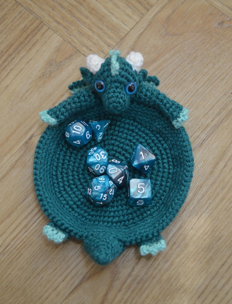 Pu&ograve; includere: Un vassoio da gioco per dadi a forma di drago in crochet color turchese con dettagli bianchi e occhietti. Il vassoio &egrave; pieno di dadi blu e bianchi con i numeri 1, 3, 4, 5, 6, 8, 9, 12, 13, 15, 18, 29, 30 e 50.