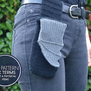 May include: A black and gray crocheted item, possibly a holster or accessory, is attached to a person's belt. The item has a textured appearance and a wing-like design. The image includes a circular graphic with text.