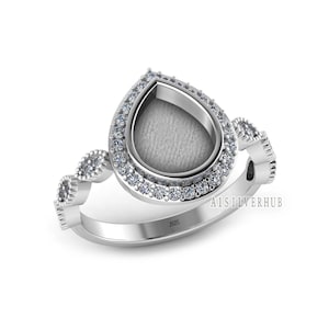 Peut inclure: Une bague en argent avec un sertissage en forme de poire, entourée d'un halo de petites pierres précieuses claires. La bande présente un motif répétitif de petits éléments décoratifs. Le texte "A1SILVERHUB" est visible.