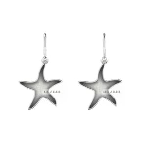 Pode incluir: Um par de brincos de estrela do mar pendentes de prata. As estrelas do mar são ocas e têm um acabamento liso e polido.