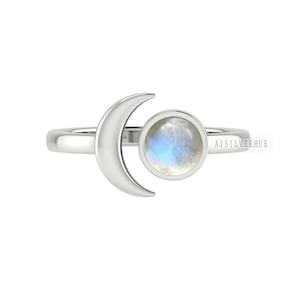 Può includere: Un anello d'argento con un design a forma di mezzaluna e una pietra di luna rotonda. L'anello è un gioiello delicato e femminile.