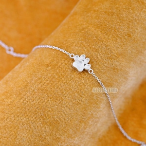 Peut inclure: Un bracelet en argent avec un pendentif en forme de patte de chien. Le pendentif est une patte de chien détaillée avec cinq orteils.