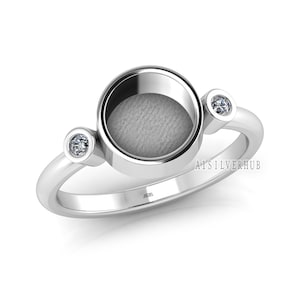May include: A silver ring featuring a round, open locket and two small, clear gemstones. The ring is hallmarked "925" and "AISILVERHUB".