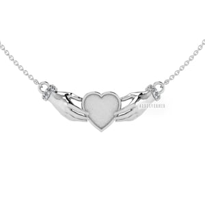 May include: Silver necklace featuring two hands holding a heart. The hands are embellished with small clear stones. The heart has a textured surface and a white finish.