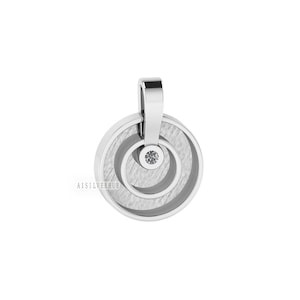 Peut inclure: Pendentif en argent avec un design circulaire texturé et une petite pierre précieuse transparente au centre.