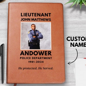 May include: A brown leather journal with a photo of a police officer and the text "Lieutenant John Matthews Andover Police Department 1981-2024 He protected. He Served."