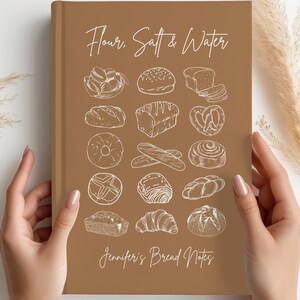 Könnte beinhalten: Ein braunes Notizbuch mit den Worten "Flour, Salt & Water" und "Jennifer's Bread Notes" in weißer Schrift. Das Cover zeigt Strichzeichnungen verschiedener Brotsorten, darunter Brotlaibe, Brötchen und Brezeln. Das Notizbuch wird von zwei Händen gehalten.