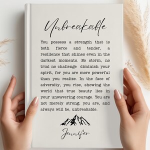May include: A white journal with the text "Unbreakable" and a quote about strength and resilience. The quote ends with "You are, and always will be, unbreakable." The journal is signed "Jennifer" and features a small mountain range illustration.