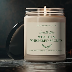 May include: A beige soy wax candle with a black lid. The candle label reads "Old Money Club" and "Smells like Wealth & Whispered Secrets". The label also states "9oz Soy Wax Candle" and "Lasts 50-60 Hours".