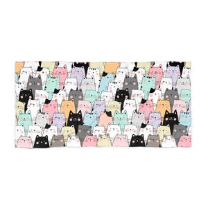 May include: A rectangular towel featuring a repeating pattern of cartoon cats in various colors including black, white, pink, blue, yellow, and grey. Each cat has simple facial features, including eyes, a nose, whiskers, and small ears.