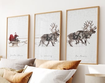 May include: Three framed prints with illustrations of reindeer pulling a sleigh. The first print says "Santa Claus", the second print says "is coming", and the third print says "to town". The prints are hanging on a white wall above a bed with brown bedding.