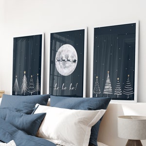 May include: Three framed prints with a dark blue background and white illustrations of Christmas trees and a full moon with Santa Claus flying in a sleigh. The text "ho ho ho!" is written below the moon.
