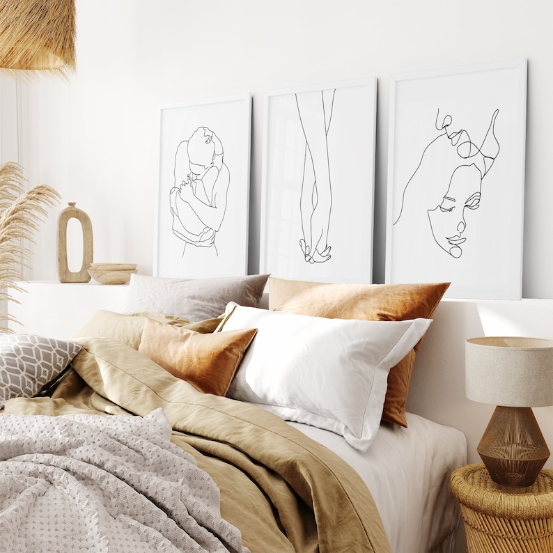 May include: Three black and white line art prints of couples in various poses. The prints are framed and hung on a white wall above a bed with brown and white bedding.