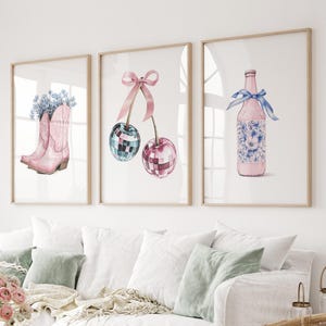 May include: Three framed watercolor illustrations. The first shows a pair of pink cowboy boots with blue flowers. The second shows two cherries with pink stems and a pink bow. The third shows a pink bottle with blue flowers and a blue ribbon.