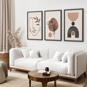 May include: Three framed abstract art prints with minimalist line drawings and muted brown and beige colors. The prints are hung on a white wall above a white sofa.