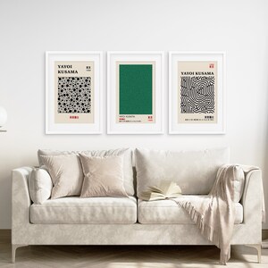 Puede incluir: Tres impresiones enmarcadas de arte abstracto de Yayoi Kusama. Las impresiones son en negro, blanco y verde. Las impresiones est&aacute;n colgadas en una pared blanca sobre un sof&aacute; blanco con almohadas beige y una manta.