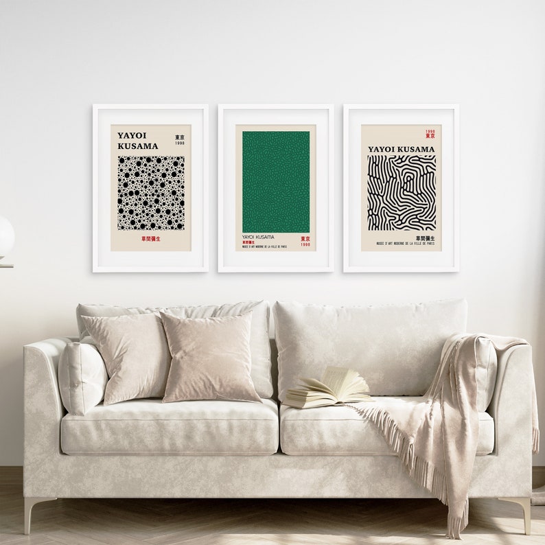 Puede incluir: Tres impresiones enmarcadas de arte abstracto de Yayoi Kusama. Las impresiones son en negro, blanco y verde. Las impresiones est&aacute;n colgadas en una pared blanca sobre un sof&aacute; blanco con almohadas beige y una manta.