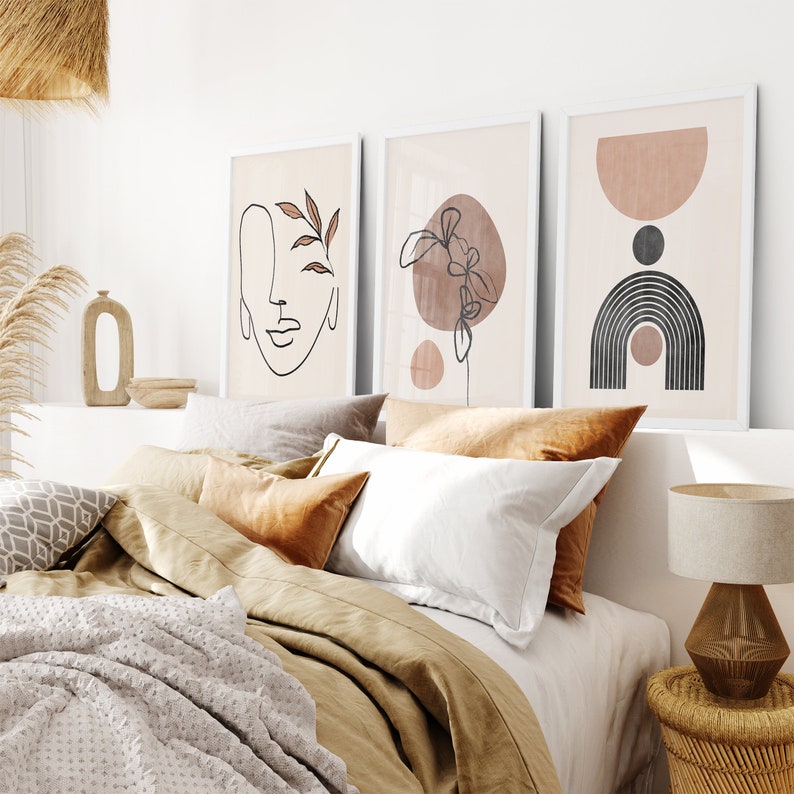 May include: Three minimalist art prints with abstract shapes and line drawings in shades of brown and black, hanging above a bed with brown and white bedding.