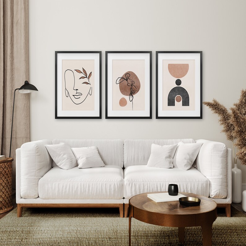 May include: Three framed abstract art prints with a minimalist style. The prints feature line drawings of a face, a flower, and geometric shapes in shades of brown and black on a light beige background.