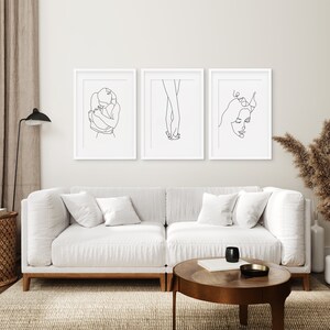 May include: Three black and white line art prints in white frames. The prints depict a couple embracing, two hands holding each other, and a woman's face.