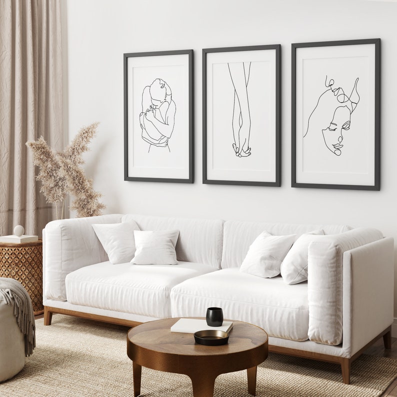 May include: Three black framed line art prints on a white wall. The prints depict a couple embracing, two hands holding each other, and a woman's face.