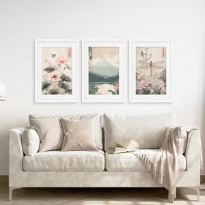 May include: Three framed prints with a Japanese theme. The left print features pink flowers and green leaves. The center print shows a mountain range with a lake in the foreground. The right print features a dragonfly and pink flowers.