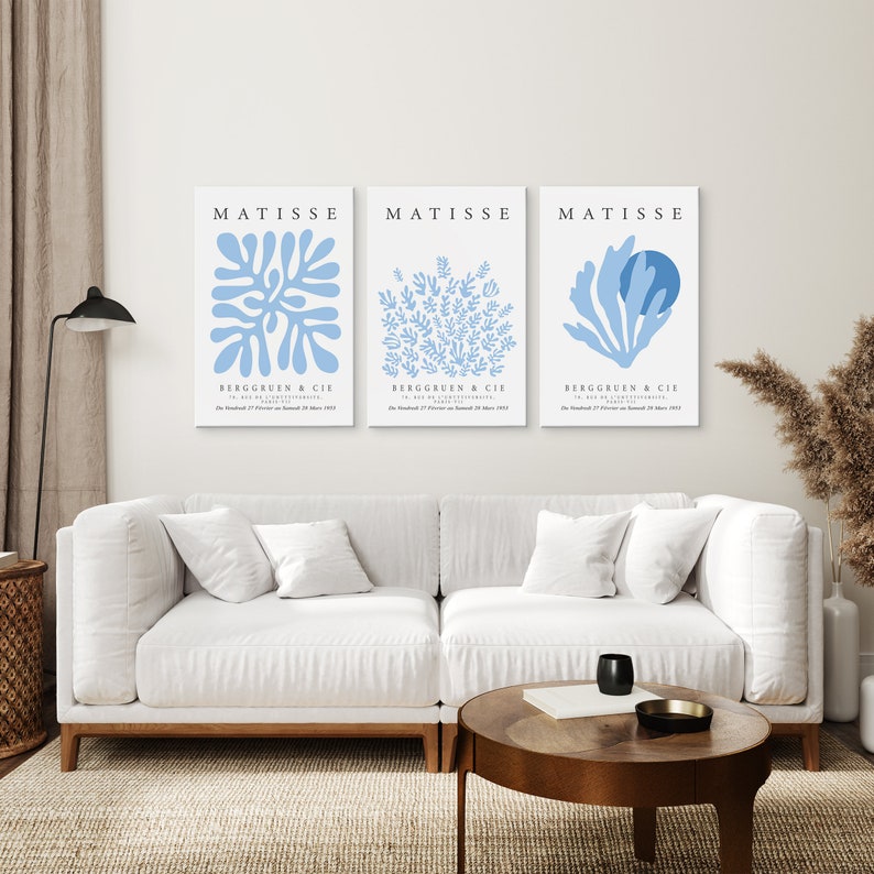以下が含まれることがあります： 白いソファと木のコーヒーテーブルのあるリビングルームに、青い白の「MATISSE」と「BERGGRUEN＆CIE」の文字が入ったマティスアートプリント3枚