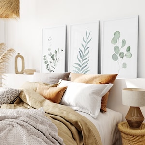 May include: A bedroom with a bed made with a brown duvet and white and brown pillows. Three framed watercolor prints of green leaves hang on the wall above the bed.