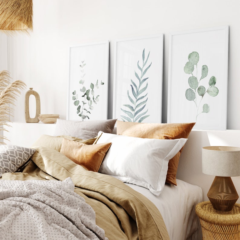 May include: A bedroom with a bed made with a brown duvet and white and brown pillows. Three framed watercolor prints of green leaves hang on the wall above the bed.