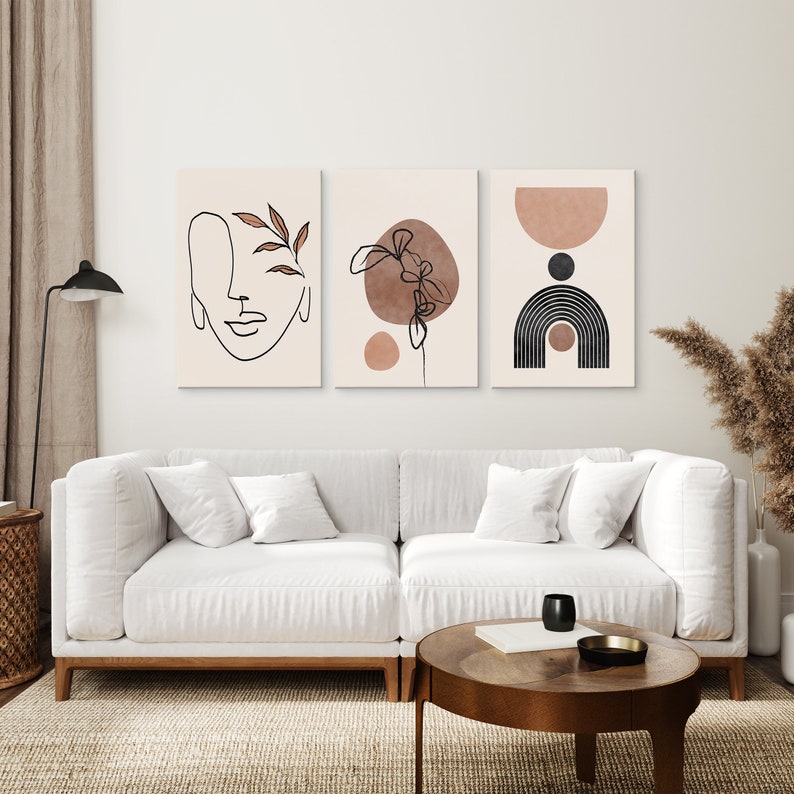 May include: Three abstract art prints in a minimalist style. The prints feature line drawings of a face, a plant, and geometric shapes in shades of brown and black on a cream background.
