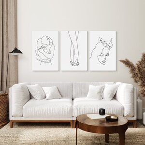May include: Three black and white line art prints depicting a couple embracing, holding hands, and a woman's face. The prints are framed and hung on a white wall above a white sofa.