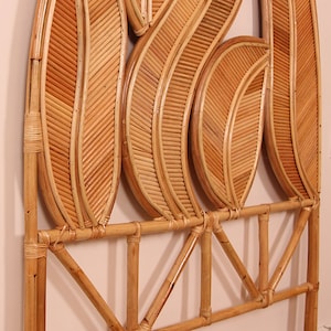 Op de afbeelding: Een natuurlijk gekleurd rotan hoofdbord met een bladeren ontwerp. Het hoofdbord heeft meerdere bladvormige elementen, elk met een gedetailleerd geweven patroon. Het frame is geconstrueerd met horizontale en schuine steunen.