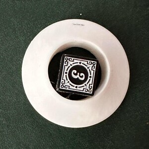 Puede incluir: Un azulejo de cerámica blanco y negro con un borde decorativo y el número "3" en el centro. El azulejo está sentado en un anillo de cerámica blanco.