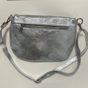 May include: A silver metallic crossbody bag with a zipper closure and a long adjustable strap.