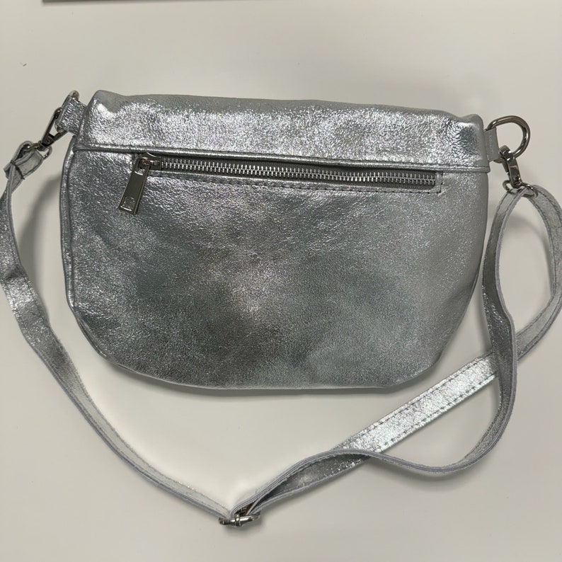 May include: A silver metallic crossbody bag with a zipper closure and a long adjustable strap.