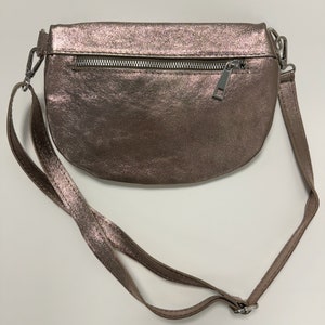 May include: A metallic rose gold crossbody bag with a zipper closure and a long adjustable strap.