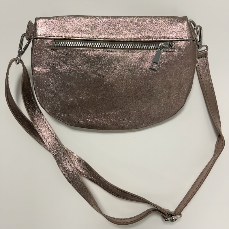 May include: A metallic rose gold crossbody bag with a zipper closure and a long adjustable strap.