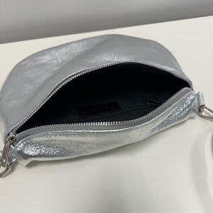 May include: A silver leather crossbody bag with a zip closure and a silver chain strap.