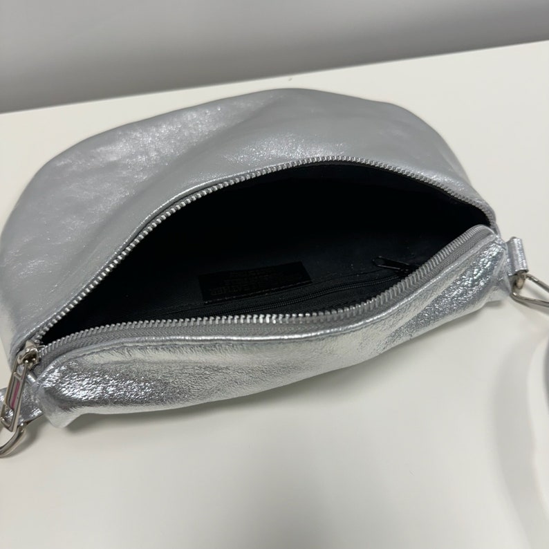 May include: A silver leather crossbody bag with a zip closure and a silver chain strap.