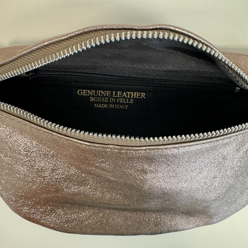May include: A silver metallic leather fanny pack with a zipper closure. The inside of the bag is black and has a label that reads "GENUINE LEATHER, BORSE IN PELLE, MADE IN ITALY."