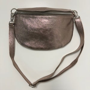 May include: A metallic rose gold fanny pack with a silver zipper and adjustable strap.