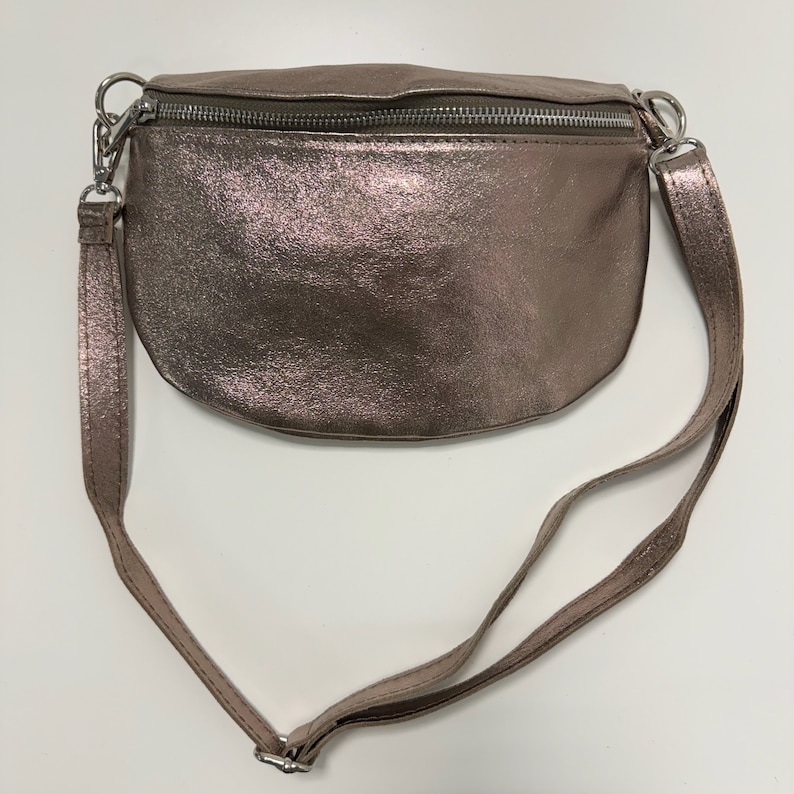 May include: A metallic rose gold fanny pack with a silver zipper and adjustable strap.