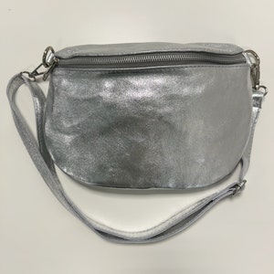 May include: A silver leather fanny pack with a white adjustable strap. The bag has a zipper closure.