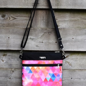 Pu&ograve; includere: Una borsa a tracolla nera con un motivo geometrico rosa e blu. La borsa ha due tasche con cerniera e una tracolla nera.